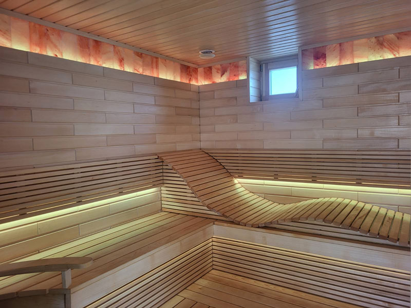 Svetlá drevená sauna s vlnitou lavicou a LED osvetlením.