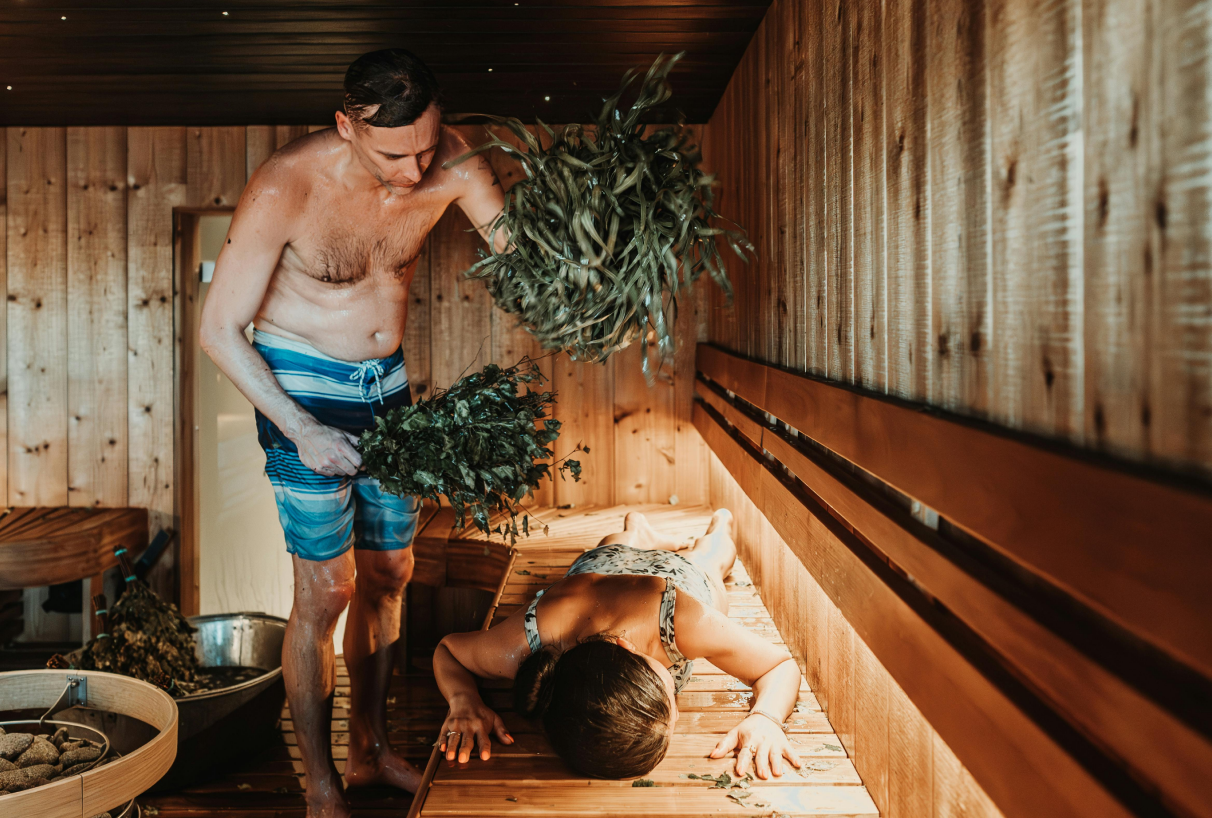Muž bije ženu brezovou metličkou v saune – tradičný saunový rituál na relaxáciu